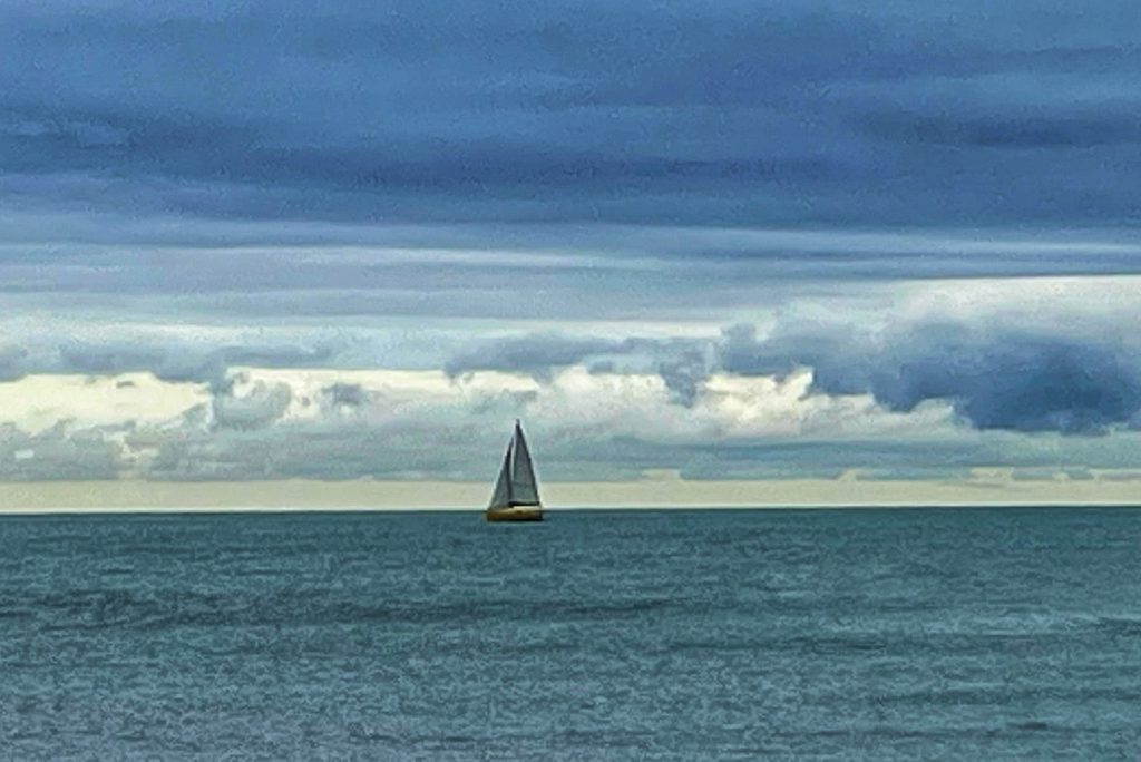 Gelbes Segelboot auf ruhigem Meer unter wolkigem Himmel – Hinweis auf die Belastung der Ozeane durch Mikroplastik
