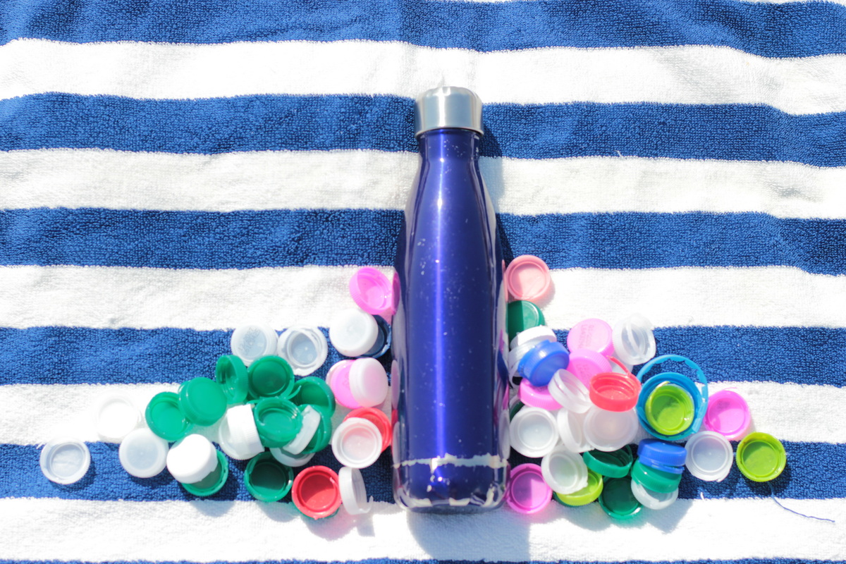 Blaue Trinkflasche neben vielen bunten Plastikdeckeln als Symbol für den alltäglichen Plastiküberfluss.