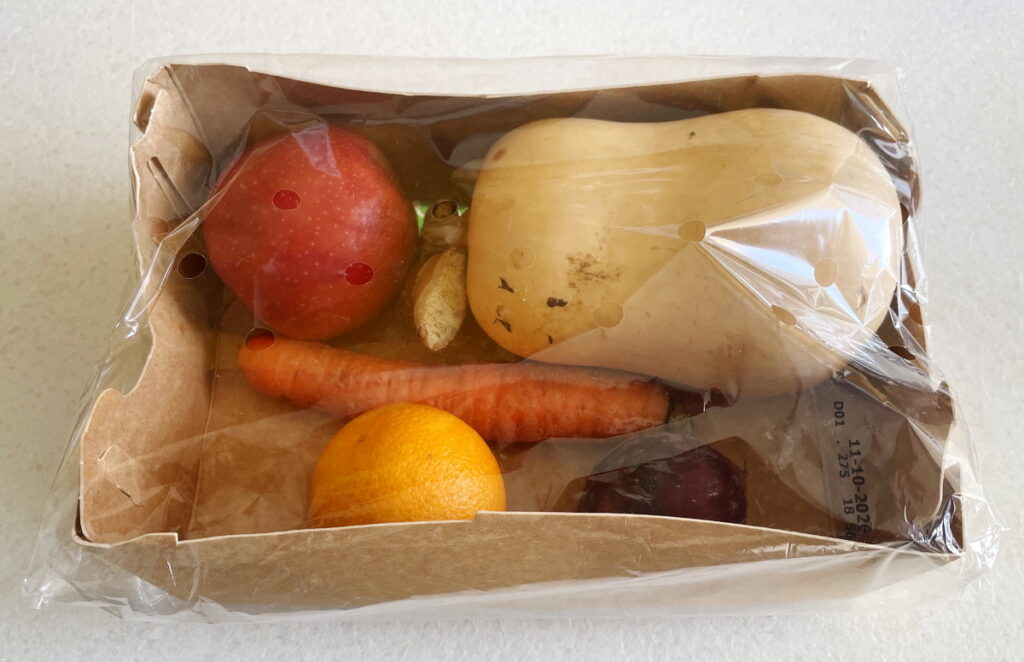 Pappschale mit Apfel, Kürbis, Karotte, Orange und weiterem Gemüse, vollständig in Plastikfolie eingeschweißt